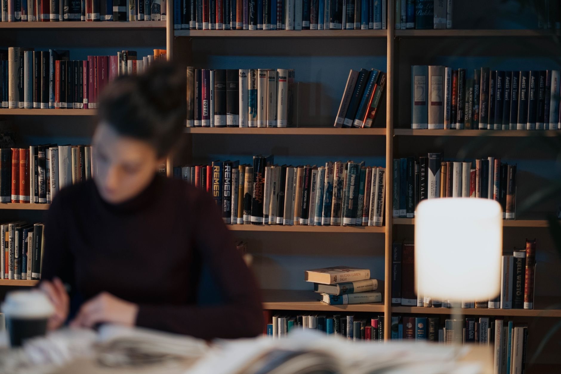 Woman studying in a library with bookshelves and warm lighting, creating a serene academic atmosphere.